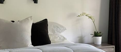A neatly made bed with white and black pillows, a white textured duvet, and a potted orchid on a bedside table.