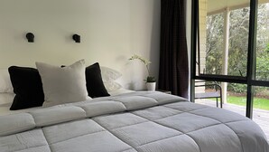 A bedroom with a large bed, white bedding, a potted plant, and a view of a garden through a window. - Kauri Park Motel (Kerikeri)