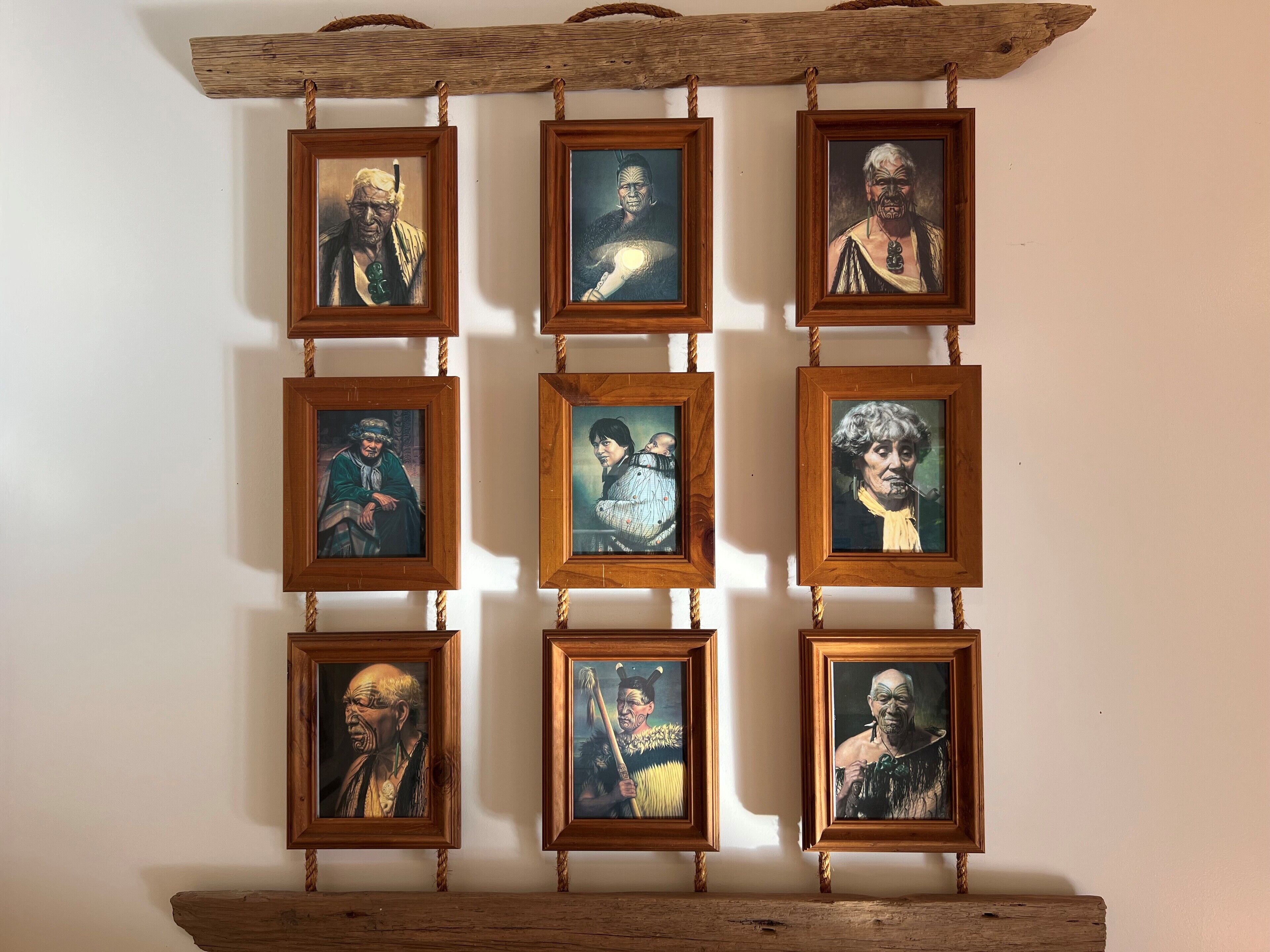 Una pared con nueve retratos enmarcados dispuestos en una cuadrícula de 3x3, cada uno con marco de madera colgado de una cuerda.