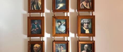 Una pared con nueve retratos enmarcados dispuestos en una cuadrícula de 3x3, cada uno con marco de madera colgado de una cuerda.