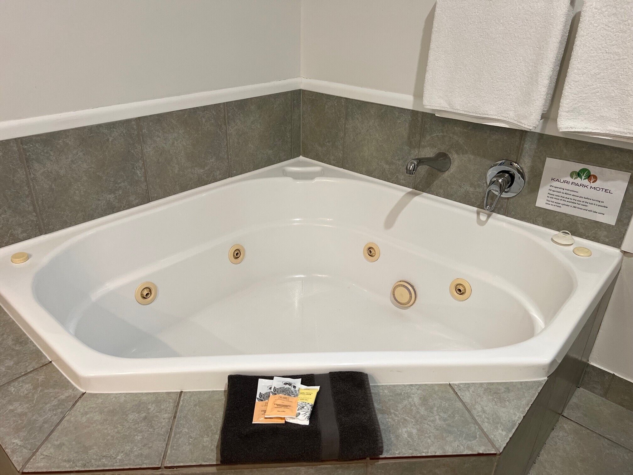 A white bathtub with four drains, a faucet, and a sign for Kauri Park Motel.