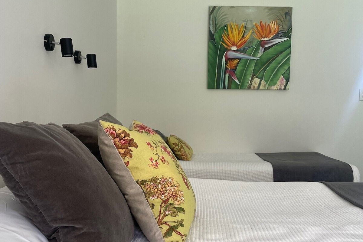 A neatly made bed with white and gray bedding, a floral pillow, and a wall-mounted light fixture.