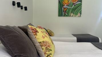 A neatly made bed with white and gray bedding, a floral pillow, and a wall-mounted light fixture.