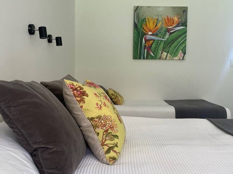 Een net opgemaakt bed met wit en grijs beddengoed, een bloemenkussen en een wandlamp.