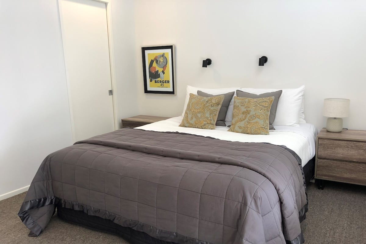 A bedroom with a bed, a nightstand, a lamp, and a framed picture on the wall.
