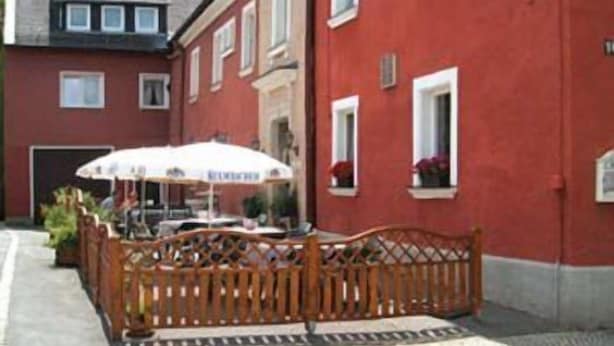 A red building with a wooden fence and a table with an umbrella. - Gasthof Rotes Roß (Zell im Fichtelgebirge)
