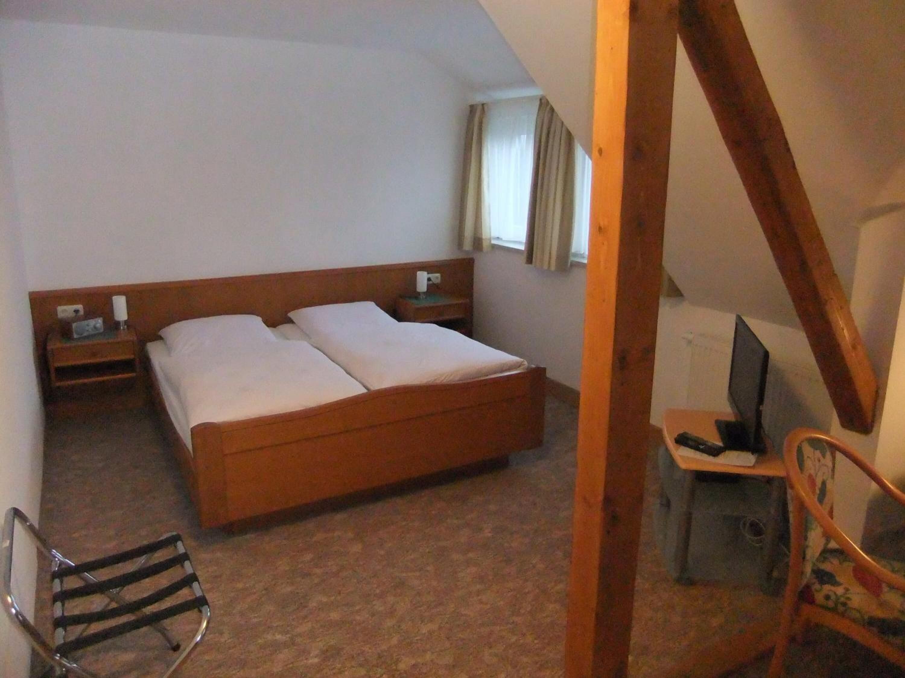Un dormitorio con una cama de madera, una mesita de noche con una radio, una silla y un escritorio con un ordenador.