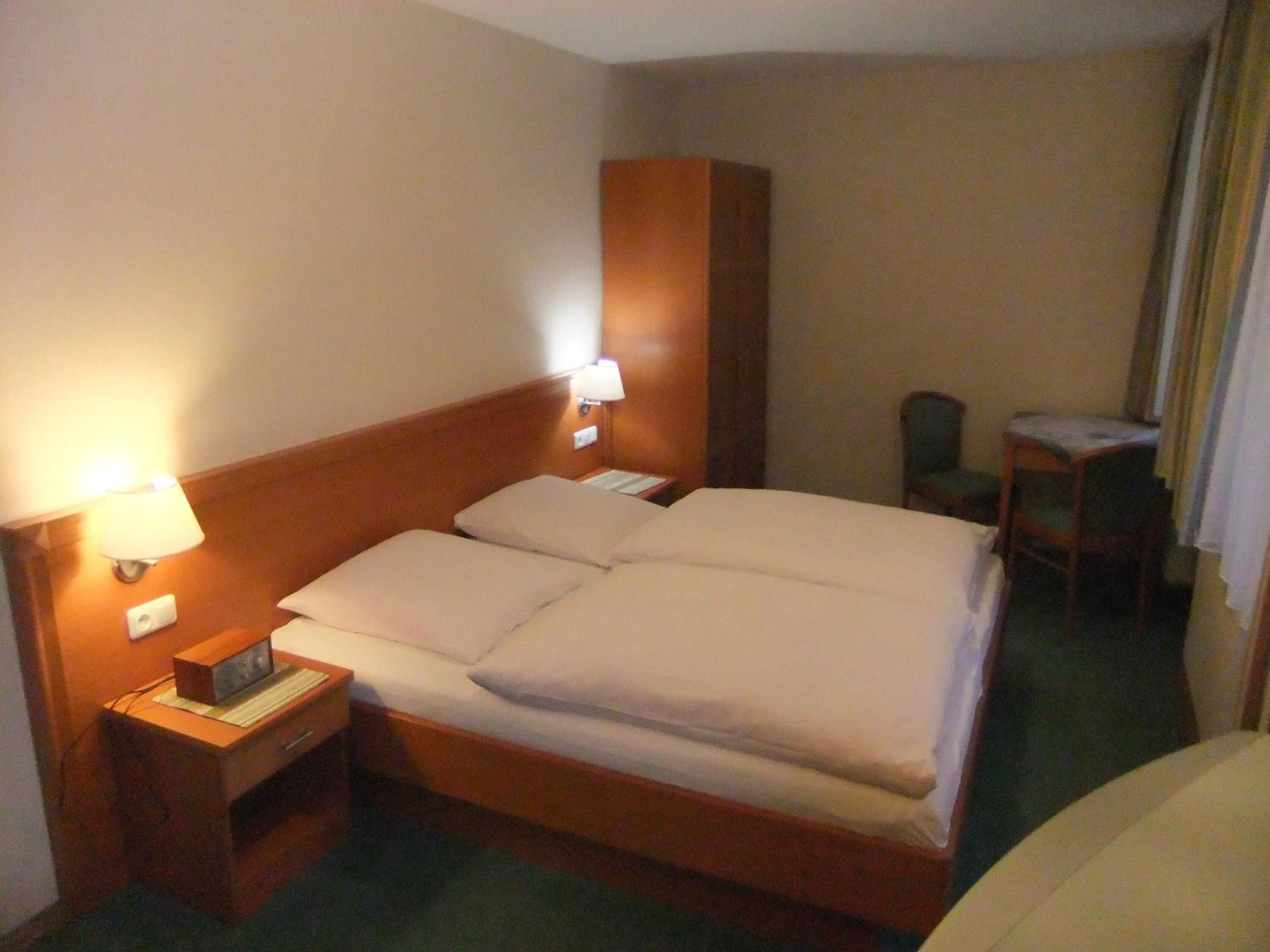 Ein Hotelzimmer mit einem Bett, Nachttischlampen, einem Nachttisch mit einer Uhr und einem Sessel.