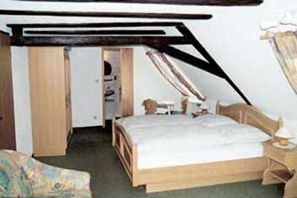 Un dormitorio pequeño y acogedor con techo inclinado, una cama de madera y una mesita de noche sencilla.