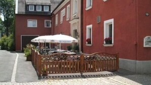 A red building with a cobblestone courtyard, a wooden fence, and a white umbrella. - Gasthof Rotes Roß (Zell im Fichtelgebirge)