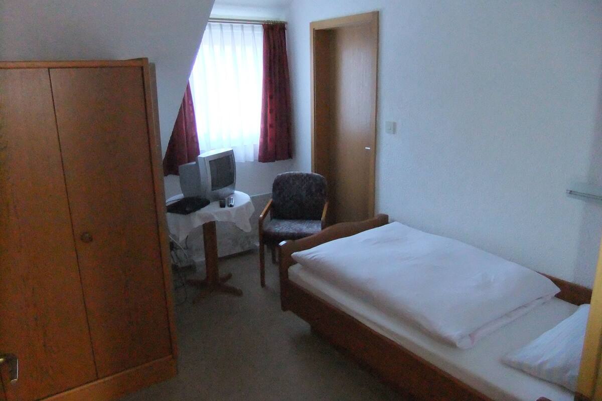Una habitación de hotel pequeña con una cama individual, un escritorio con silla, televisor y armario.