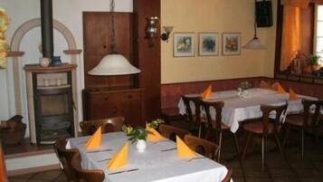 A restaurant with wooden furniture, white tablecloths, and yellow napkins. There is a wooden cabinet, a hanging lamp, and framed pictures on the wall.