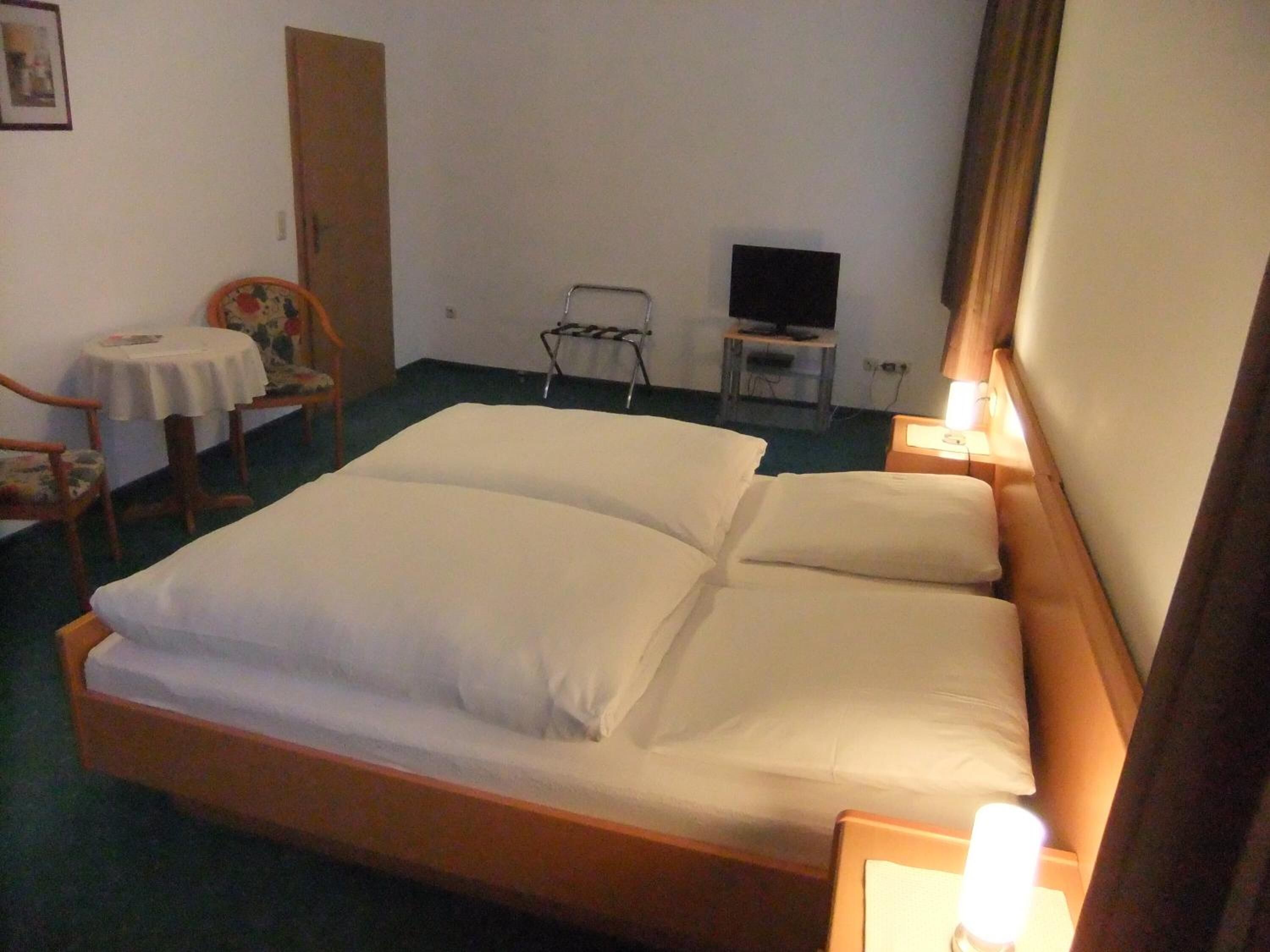 A hotel room with a single bed, a small table with a chair, a TV, and a bedside lamp.