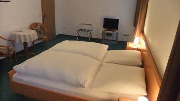 Camera d'albergo con un letto singolo, un tavolino con una sedia, una televisione e una lampada da comodino.