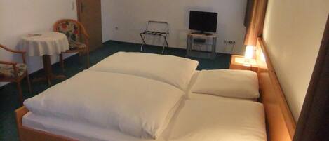 A hotel room with a single bed, a small table with a chair, a TV, and a bedside lamp.
