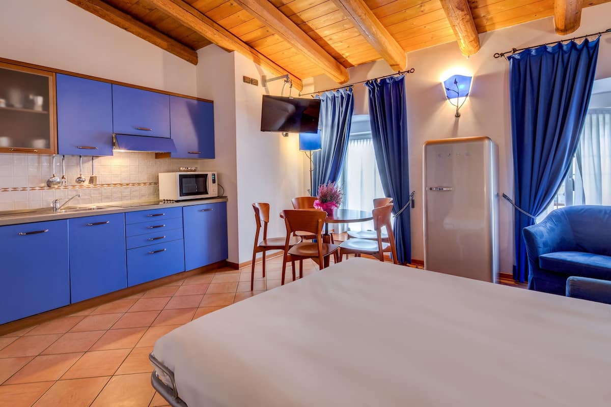Une pièce comprenant un lit, une table à manger avec des chaises, une cuisine avec des placards bleus, un four à micro-ondes et un téléviseur fixé au mur.