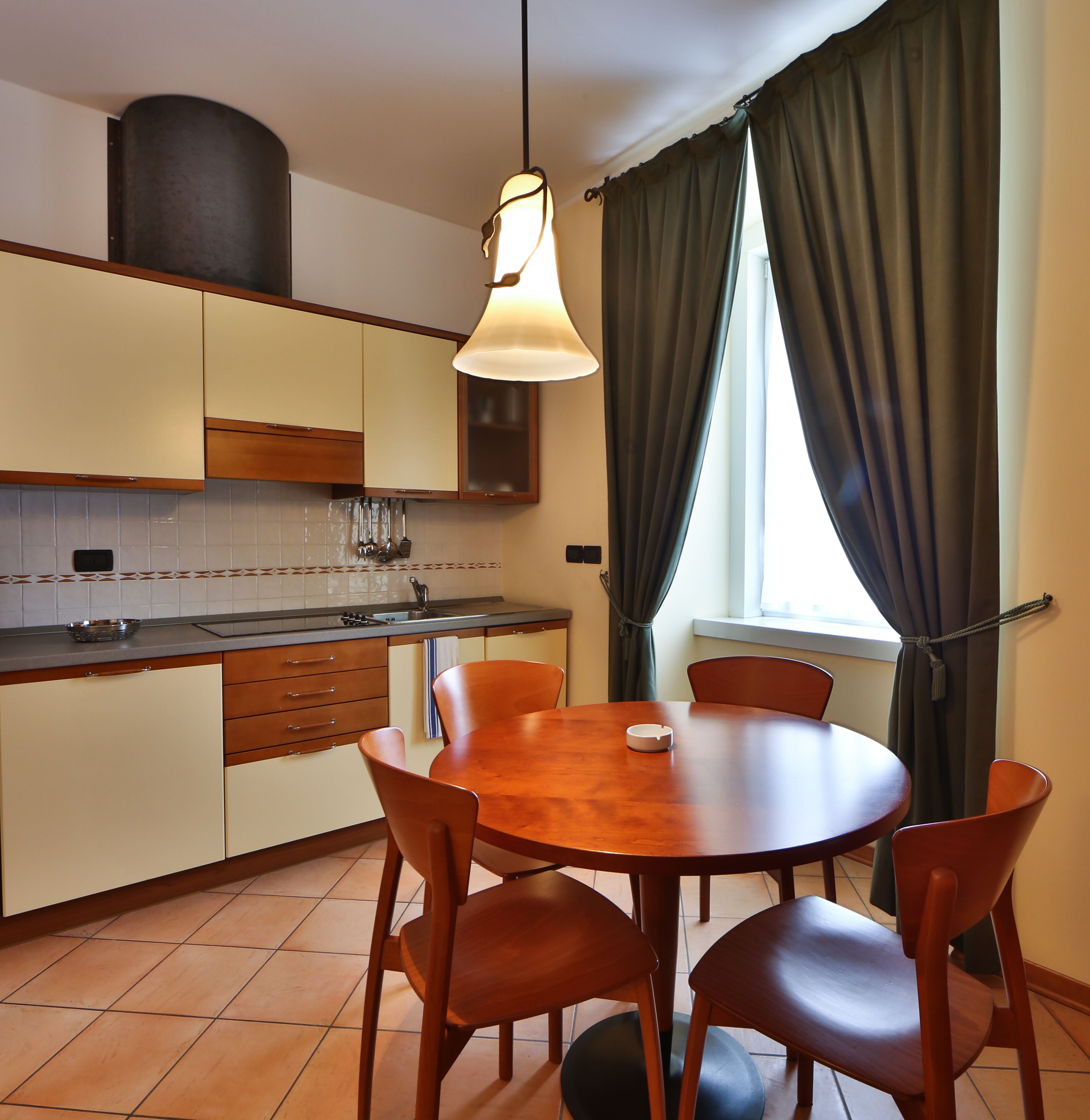 Una cocina moderna con una mesa redonda de madera y seis sillas, una lámpara colgante y una ventana con cortinas.