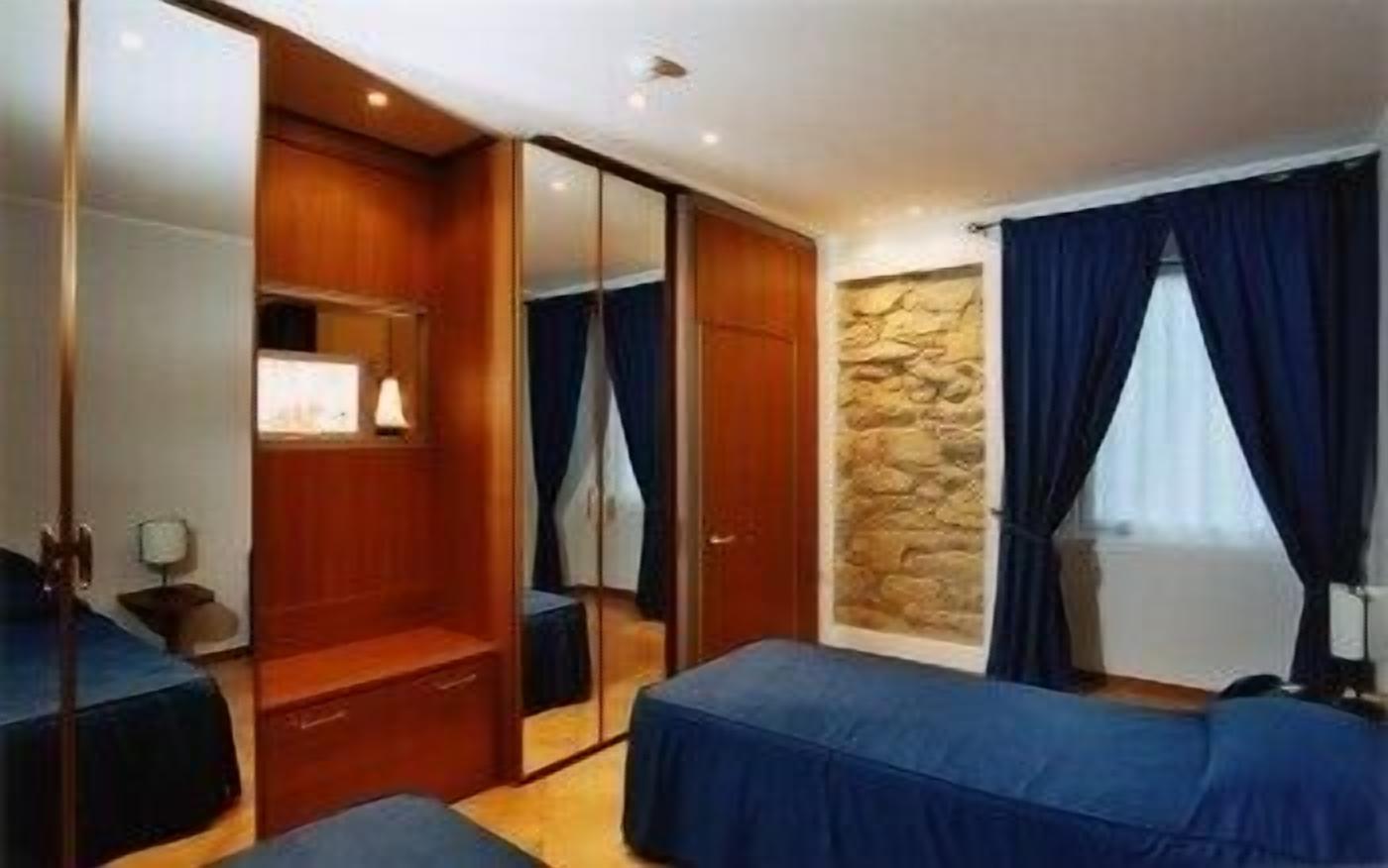 Camera d'albergo con armadio, un letto, uno specchio, una parete in pietra e una finestra con tende.
