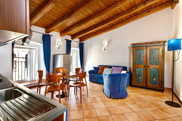 A spacious living area with a wooden ceiling, a dining table with chairs, a blue sofa, and a cabinet with decorative doors.