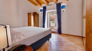 Un dormitorio con cama, teléfono en la mesita de noche, armario de madera y ventana con cortinas.