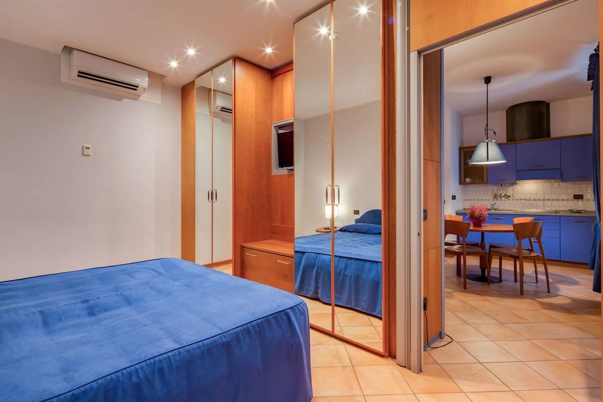 Une chambre avec deux lits, un miroir, une armoire et, au fond, un coin cuisine.