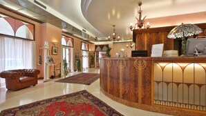 Un vestíbulo de hotel con mostrador de recepción, un sofá de cuero, una araña y una alfombra grande con motivos.