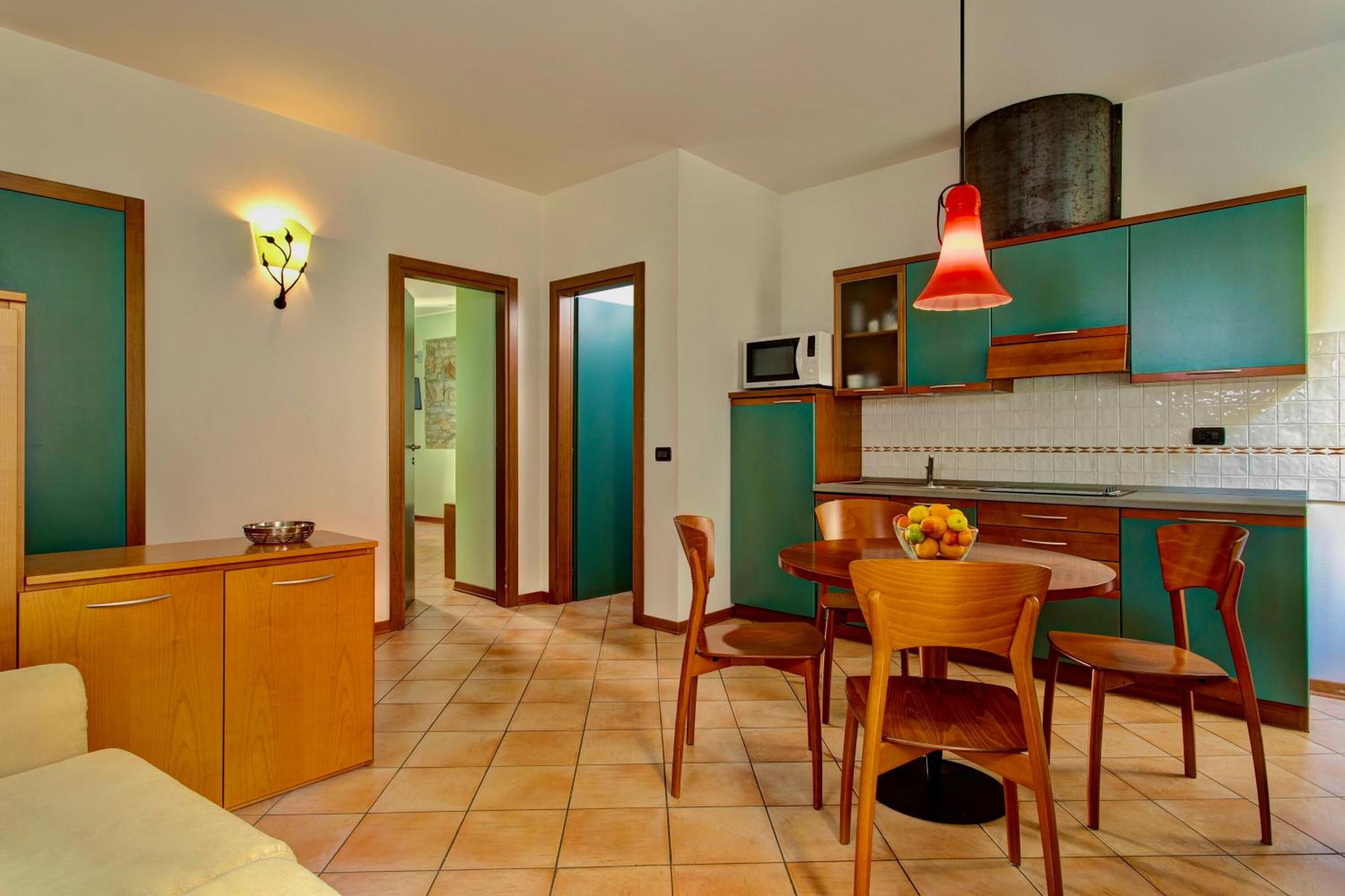 Une cuisine moderne avec des meubles de couleur verte, un four à micro-ondes et un coin repas comprenant des chaises et une table en bois.