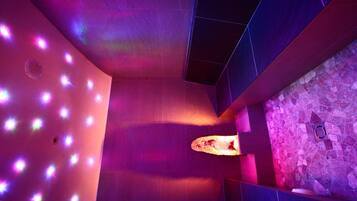 Ein modernes Badezimmer mit Steinwand, Waschbecken und einer Decke mit violetter Beleuchtung.