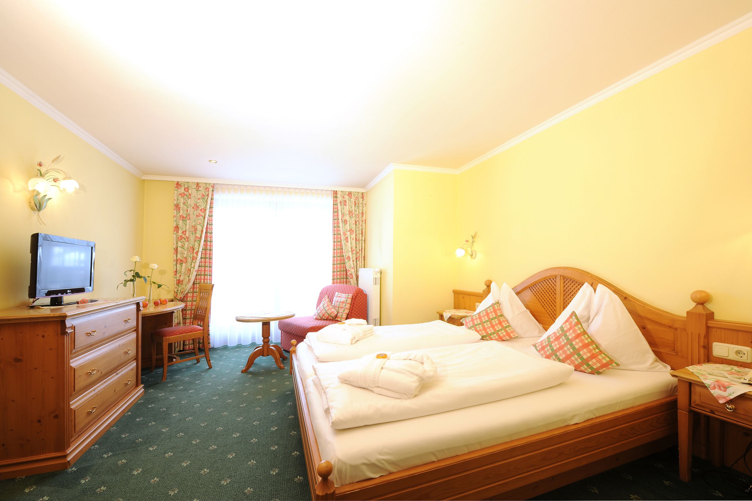 Habitación de hotel con cama, escritorio, silla, televisor y ventana con cortinas.