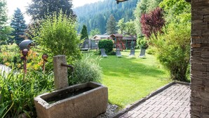 A garden with a stone planter, a wooden structure, and a view of a forested area. - Aparthotel Kristall (Altenmarkt im Pongau)