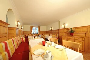 A hotel dining area with long communal tables, wooden paneling, and a red carpeted floor. - Aparthotel Kristall (Altenmarkt im Pongau)