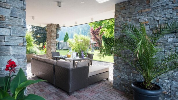 An outdoor patio area with stone walls, a wicker sofa set, and a potted plant. - Aparthotel Kristall (Altenmarkt im Pongau)