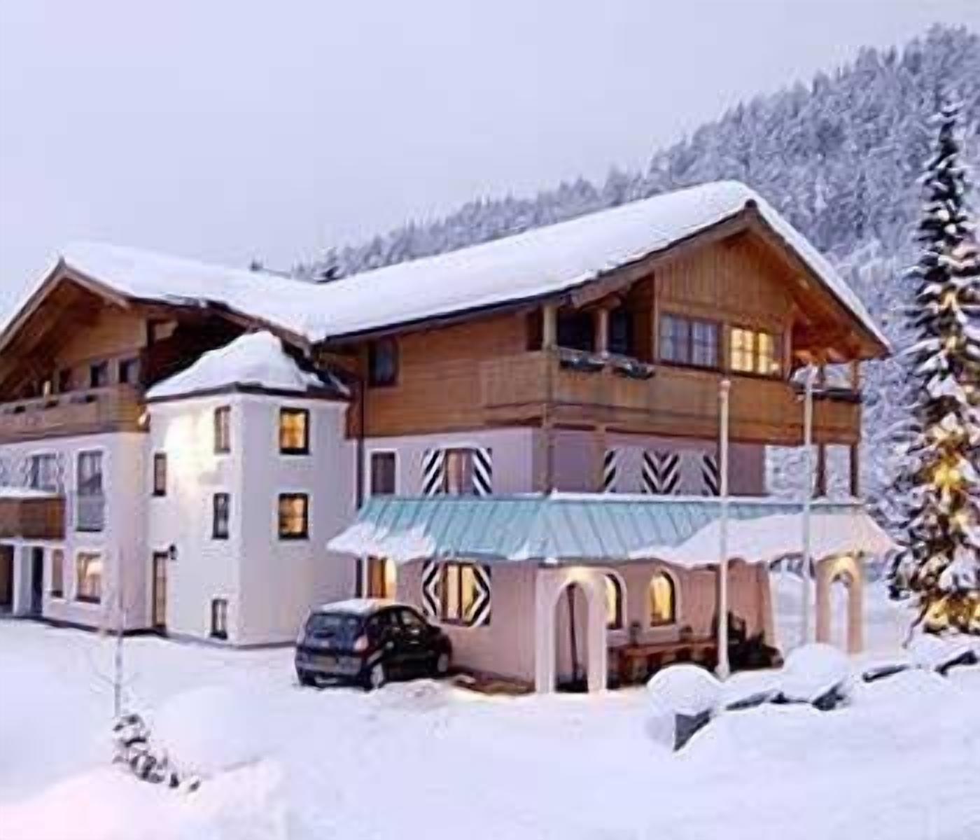 A large wooden building with multiple balconies and a covered entrance, surrounded by snow-covered trees.