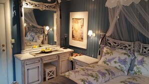 A bedroom with a large ornate mirror, a bedside table with a lamp, a framed artwork on the wall, and a canopy bed with floral bedding. - Solheim Overnatting (Midt-Telemark)