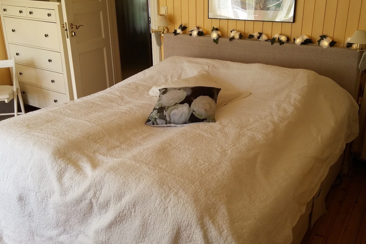 A neatly made bed with a floral pillow, a bedside lamp, and a wall-mounted telephone.