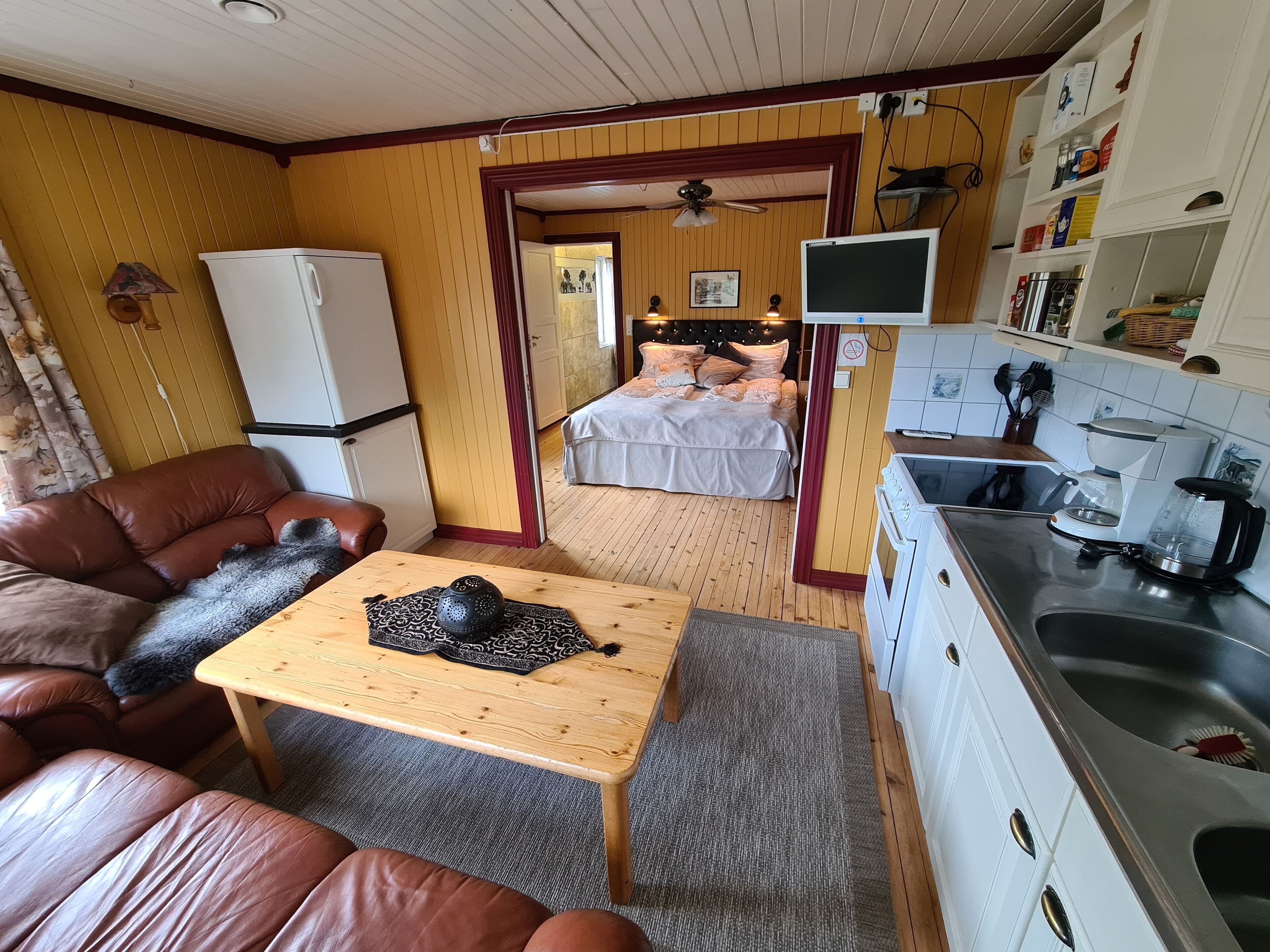 A compact living space with a sofa, a small table, a bed, a kitchenette, and a ceiling fan.