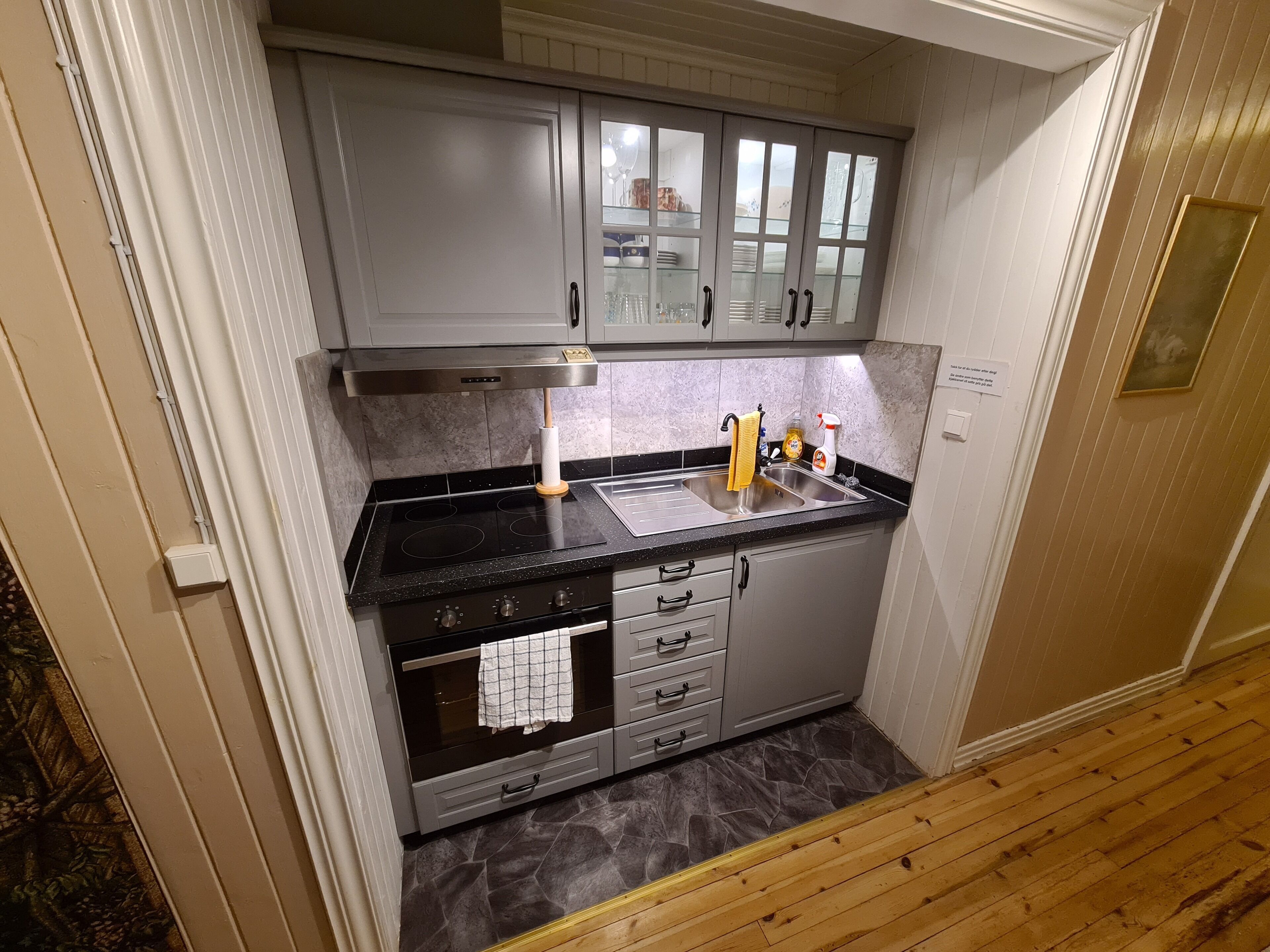 A compact kitchen with a black countertop, stainless steel sink, and a built-in oven.