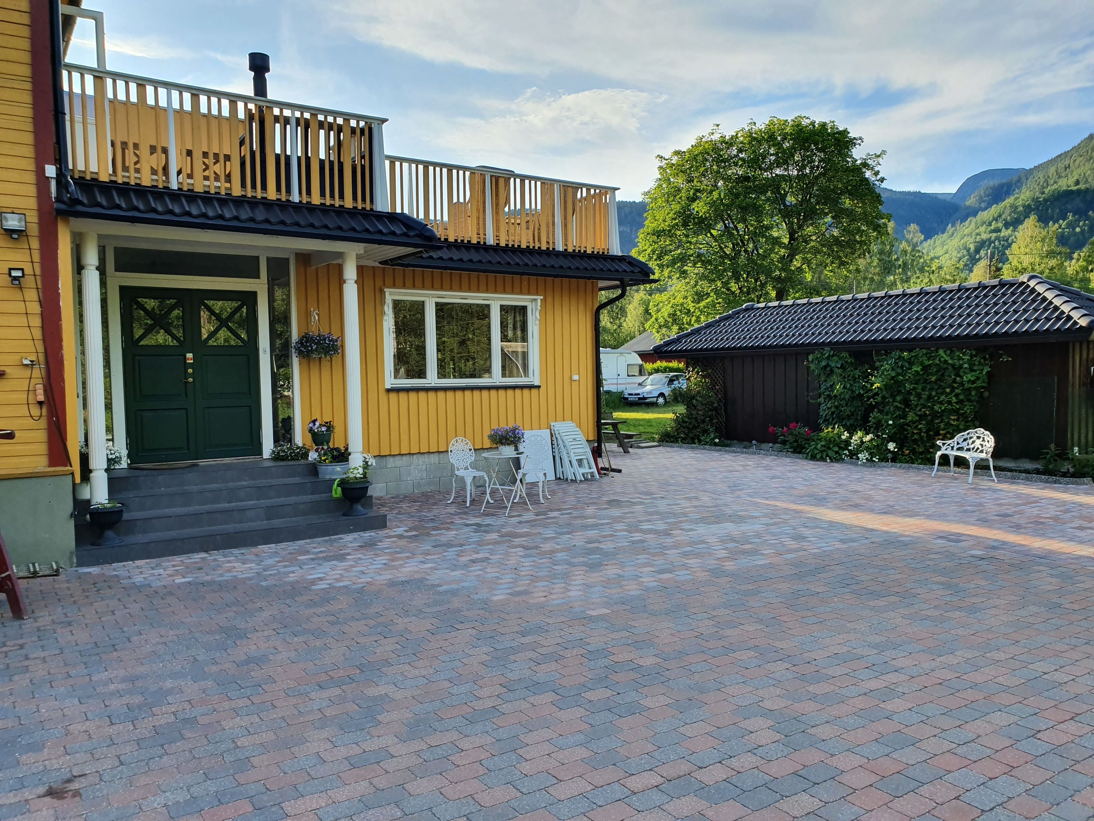 A yellow building with a green door, a balcony, and a paved courtyard with chairs and tables.