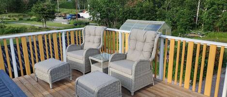 A wooden deck with wicker furniture and a glass enclosure.