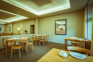 Un comedor de hotel con varias mesas y sillas de madera, un cuadro en la pared y piso alfombrado.