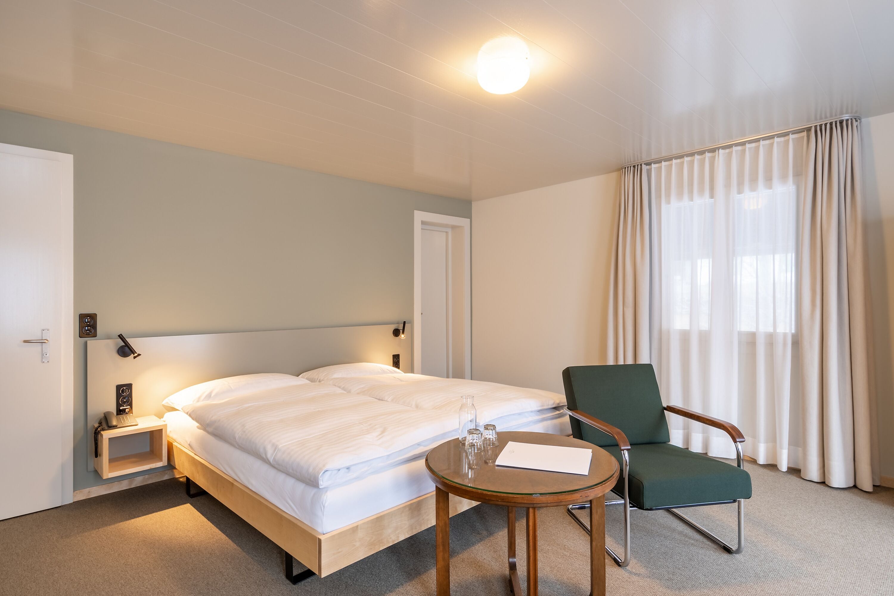 A hotel room with a bed, a chair, a small table, and a nightstand.
