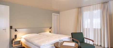 A hotel room with a bed, a chair, a small table, and a nightstand.
