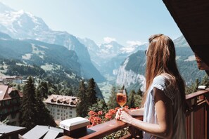 A person holding a glass of drink, overlooking a mountainous landscape with buildings in the valley. - Hotel Alpenruhe - Vintage Design Hotel (Lauterbrunnen)