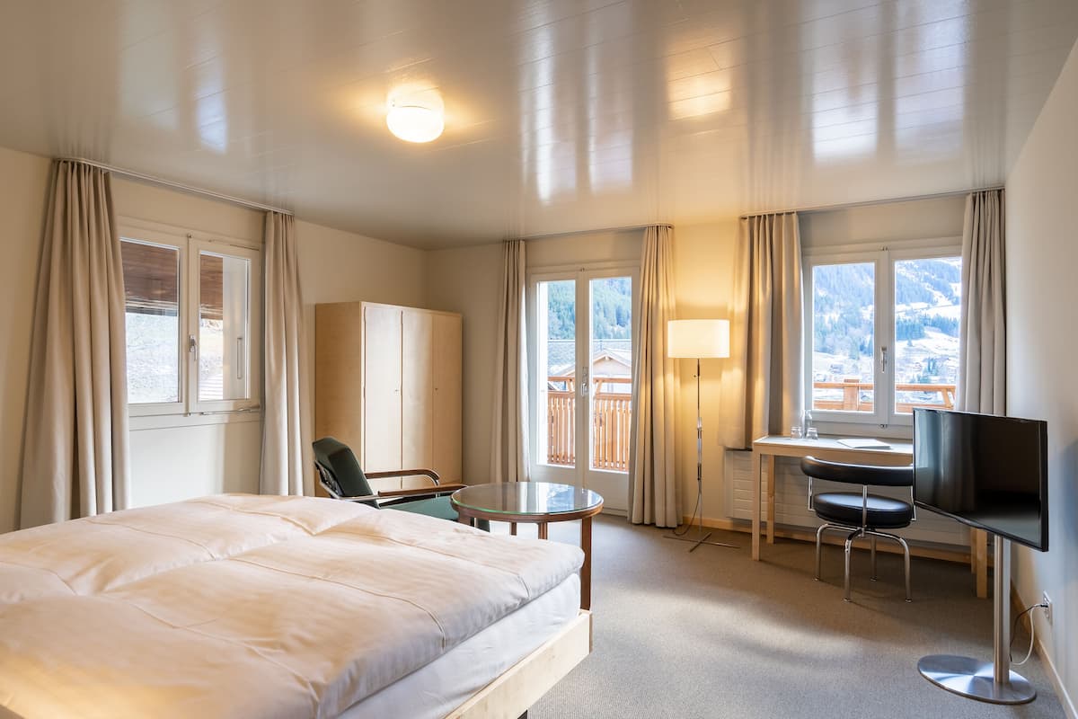 Ein Hotelzimmer mit Bett, Schreibtisch, Sessel und Fernseher, mit Blick auf die Berge.