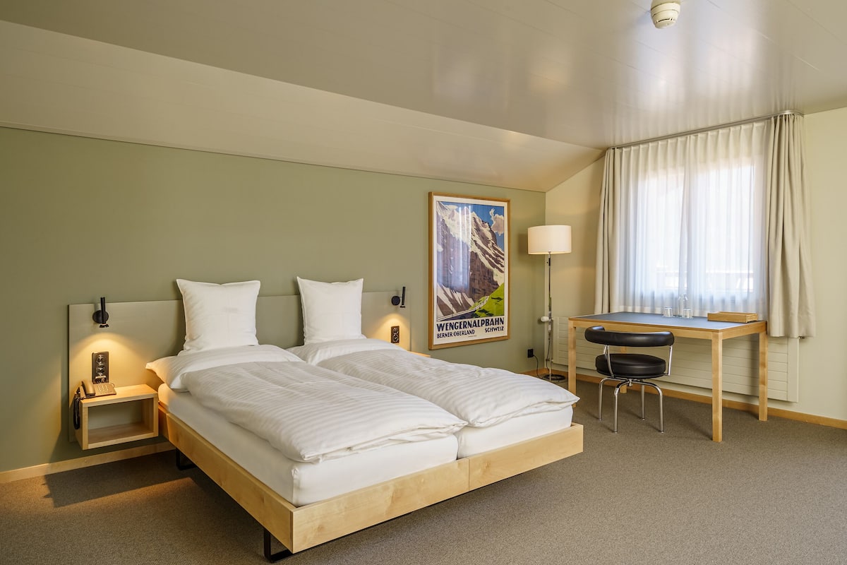 Ein Hotelzimmer mit Doppelbett, Nachttischen mit Lampen, einem Schreibtisch und einem Stuhl sowie einem Poster an der Wand.