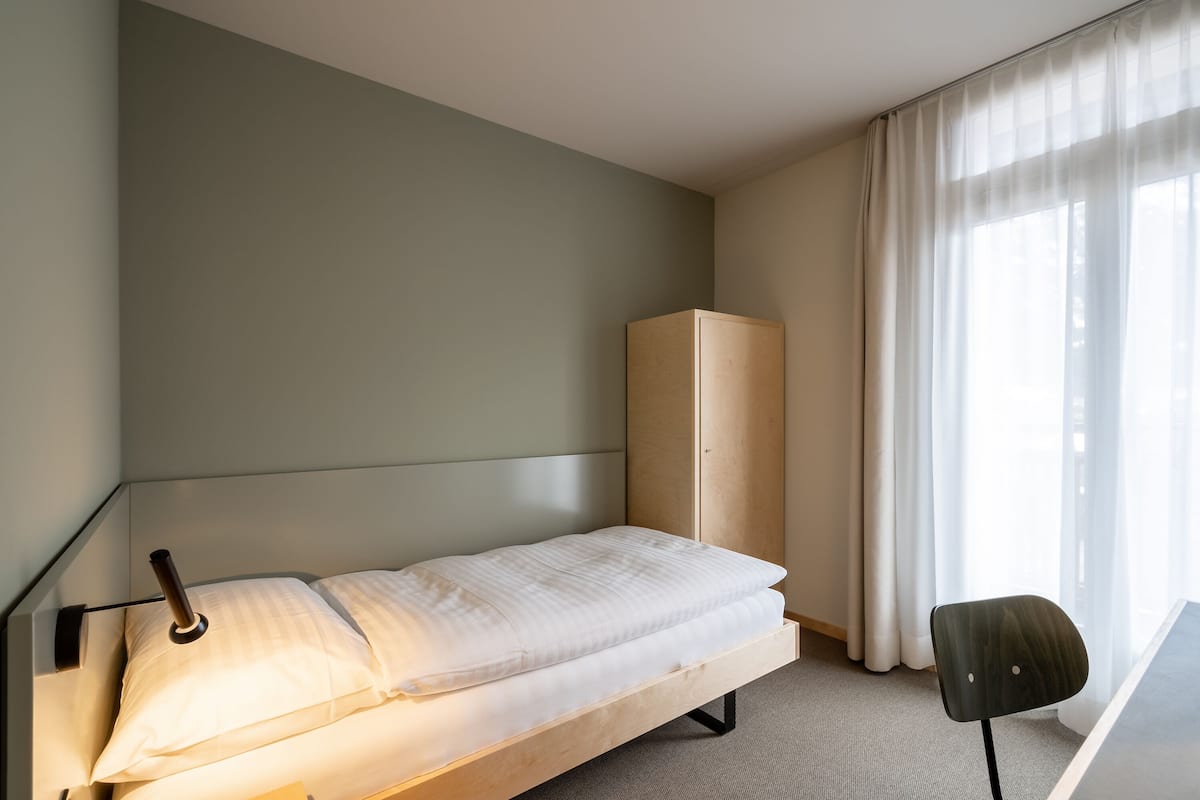 Ein schlicht eingerichtetes Hotelzimmer mit einem Bett, einem Kleiderschrank und einem Schreibtisch mit Stuhl.