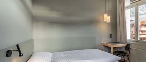 A hotel room with a single bed, a desk, a chair, a lamp, and a window with curtains.