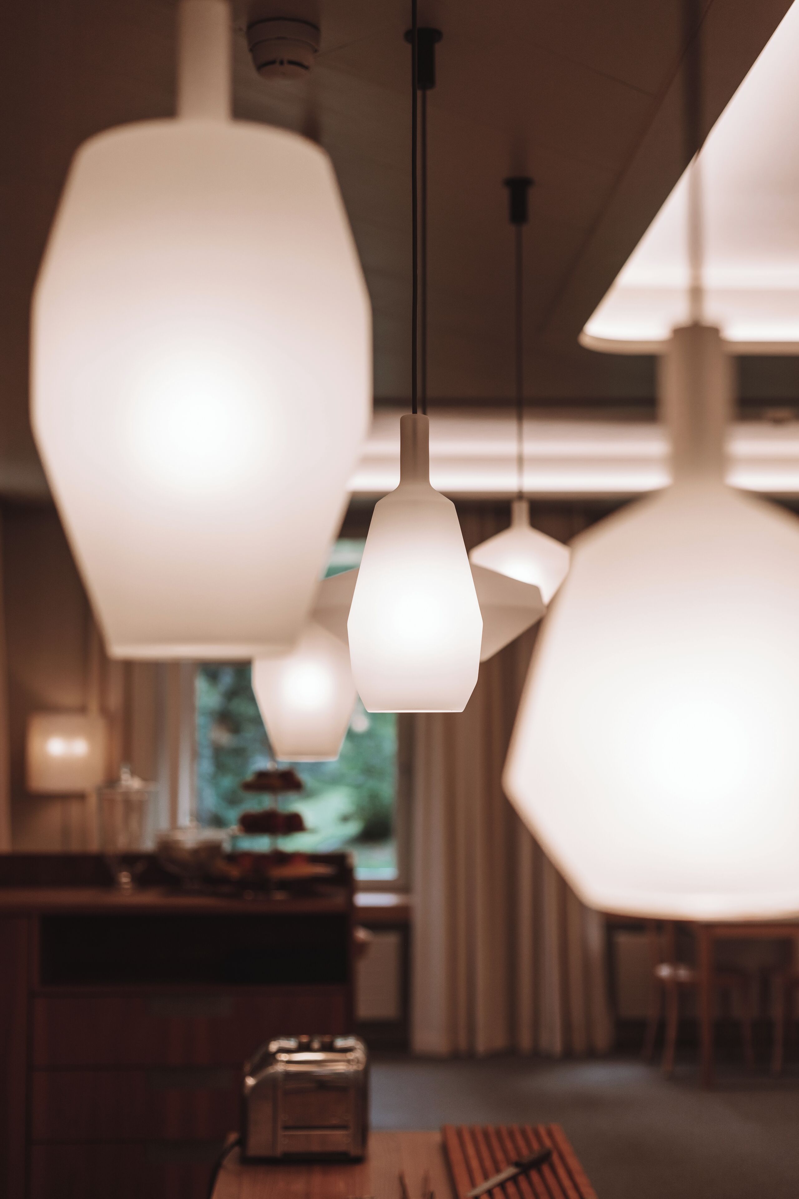 A modern interior with pendant lighting, a wooden table, and a view of the outdoors.