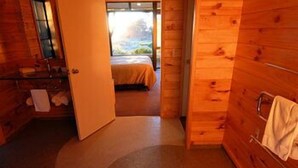 A wooden cabin interior with a spiral carpet, a bed, and a bathroom with a towel hanging on the door. - Beach Hideaway (Barrytown)