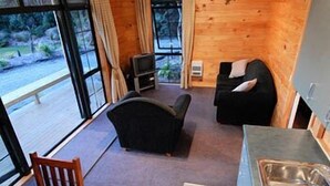 A compact cabin with a wooden interior, a sofa, a television, and a dining area with a table and chairs. - Beach Hideaway (Barrytown)